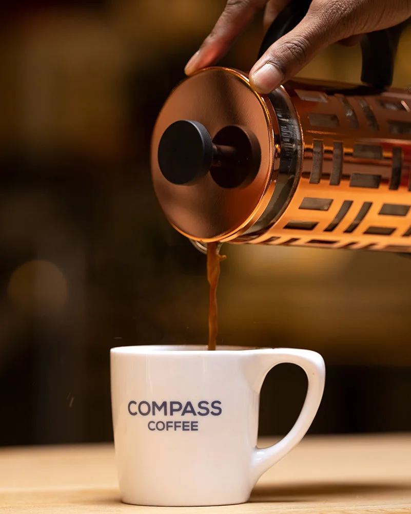 Dark roast Compass Coffee poured from a French press into a Compass mug