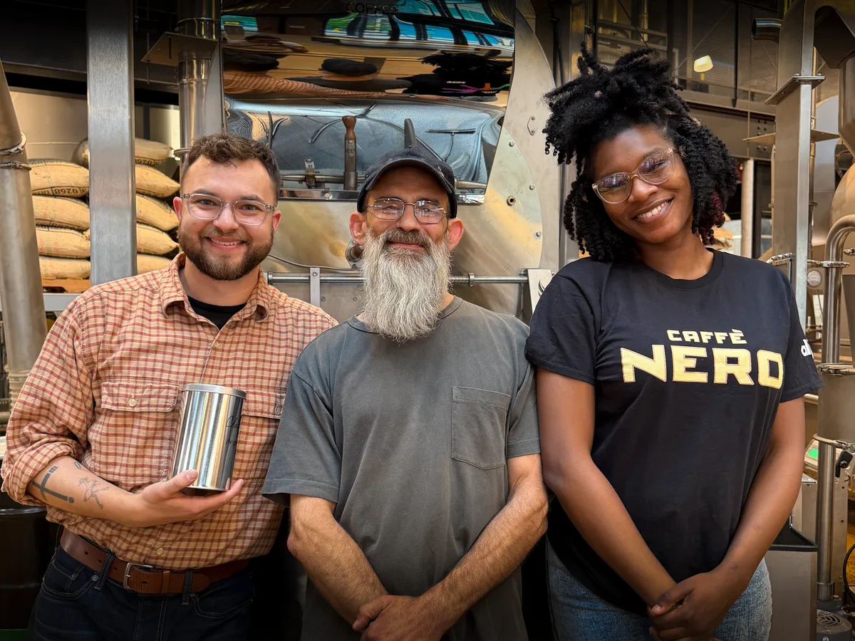 Three members of the Compass Coffee team at the roastery, one holding a coffee tin