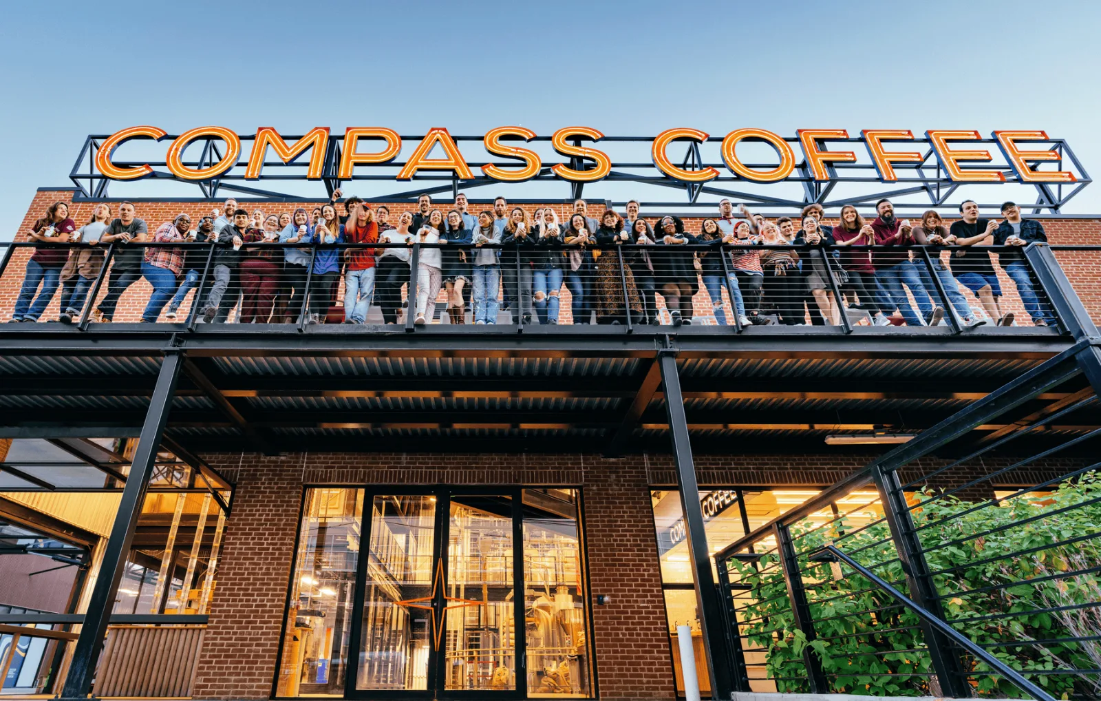 The Compass Coffee team on the balcony of the Ivy City roastery, under the Compass Coffee sign