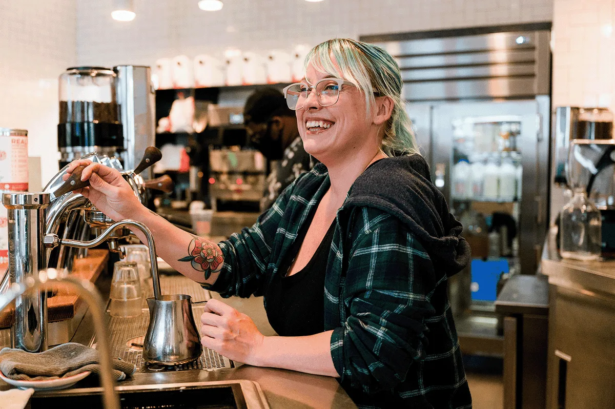 A Compass Coffee barista smiling behind the espresso bar