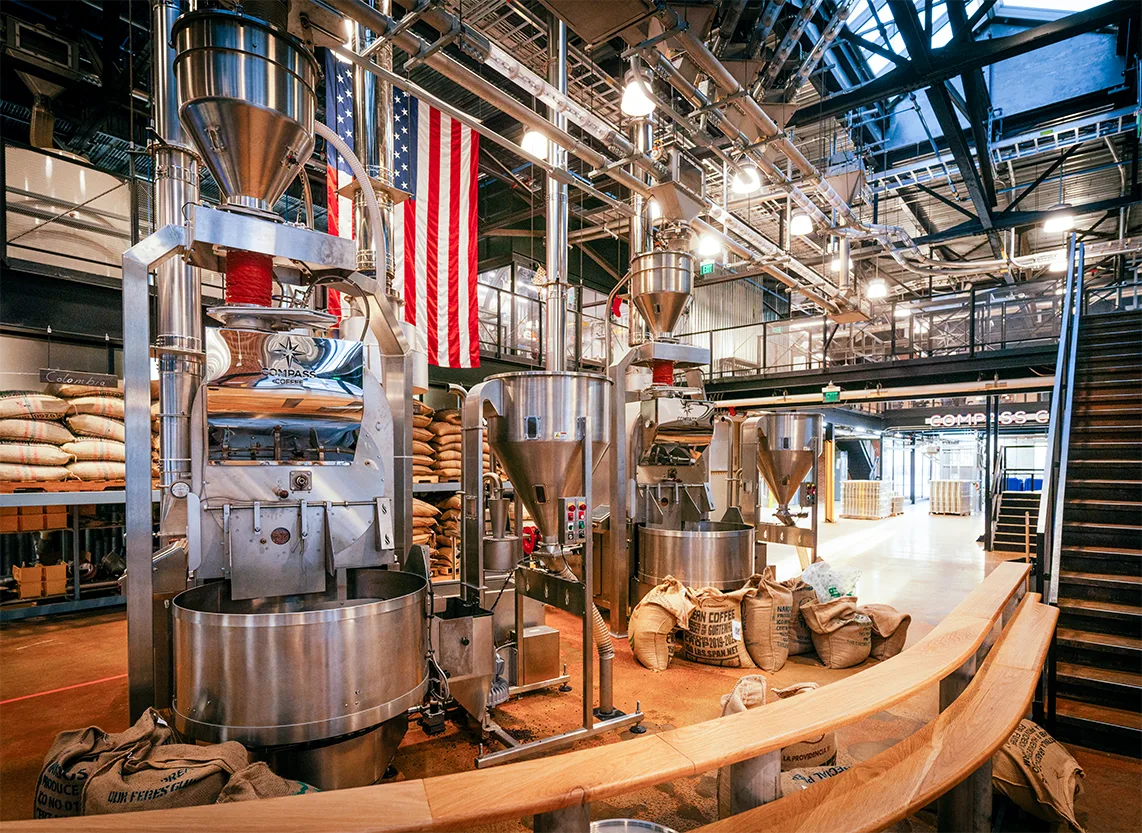 Inside the Compass Coffee Ivy City roastery, with roasters and an American flag