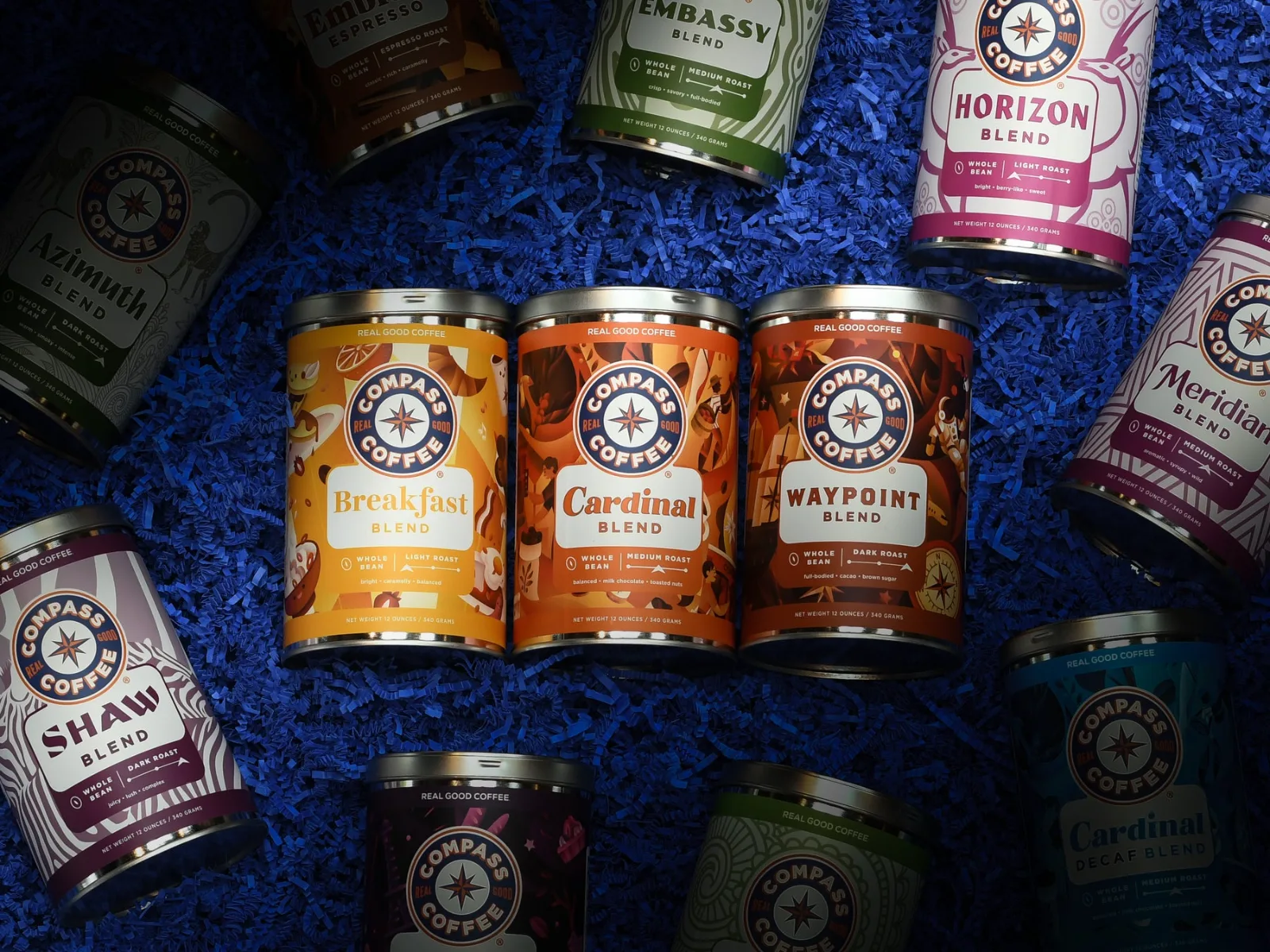 Compass Coffee tins laid out on blue paper: Breakfast, Cardinal, Waypoint, Shaw, Embassy and Horizon